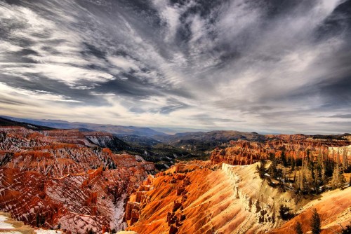 A panoramic view of colorful rock formations and valleys under a dramatic sky, showcasing nature's beauty.