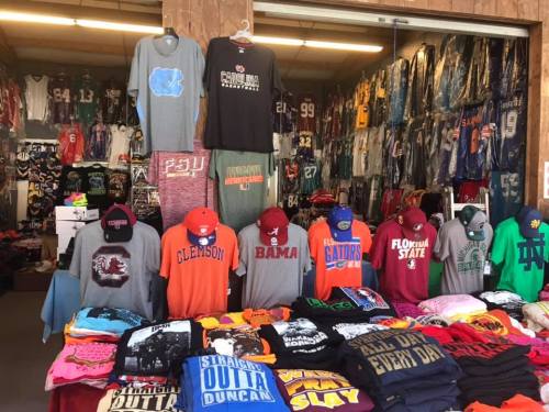 A display of colorful t-shirts and hats featuring various college sports teams in a shop.