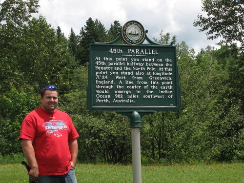 A man stands next to a sign marking the 45th parallel, halfway between the Equator and the North Pole.