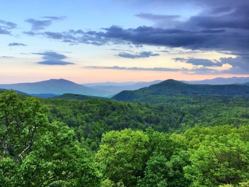 A scenic view of lush green mountains under a colorful sky at dusk, with clouds scattered above.