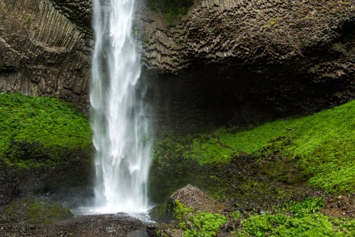 A cascading waterfall flows over rocky cliffs, surrounded by lush green vegetation.