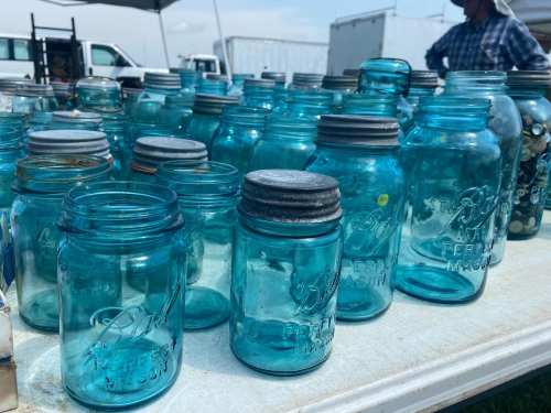 A collection of vintage blue glass jars displayed on a table at an outdoor market.