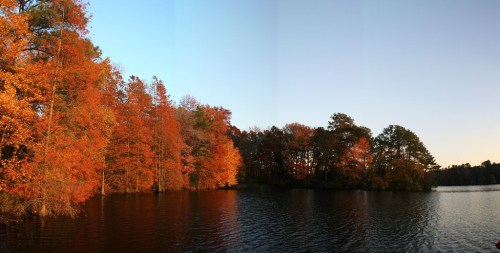 A serene lake surrounded by vibrant autumn trees reflecting orange and yellow hues in the calm water.
