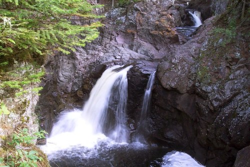 A serene waterfall cascading over rocky terrain, surrounded by lush green foliage and a tranquil pool below.