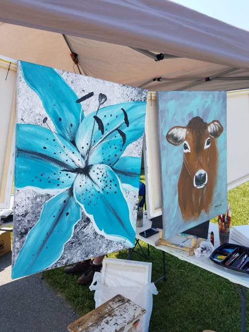 Two paintings displayed under a tent: one of a blue flower and the other of a brown cow.