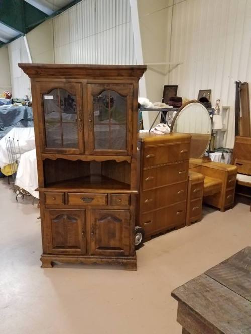 A wooden display cabinet with glass doors, next to a dresser and other vintage furniture in a spacious room.