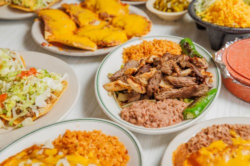 A variety of Mexican dishes including tacos, rice, beans, and grilled meat, all served on colorful plates.