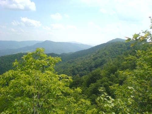 Lush green mountains under a blue sky with scattered clouds, showcasing a serene natural landscape.