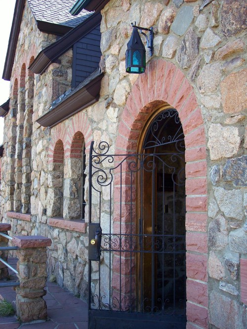 A stone building with arched windows and a decorative wrought iron gate, featuring a lantern above the entrance.