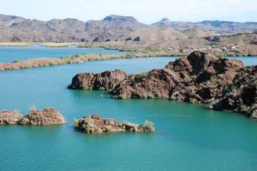 A serene landscape featuring a turquoise lake surrounded by rocky hills and sparse vegetation under a clear sky.