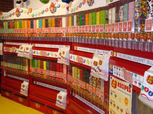 A colorful display of jelly beans in various flavors, arranged in clear containers on a red shelf.