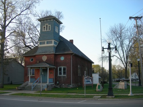 Historic building with a blue tower, red brick facade, and a sign, set in a quiet street with trees and streetlights.