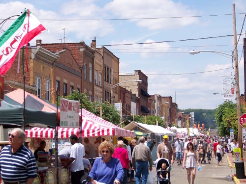 A bustling street market with colorful tents, vendors, and crowds enjoying a sunny day.