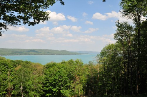 A serene lake surrounded by lush green trees under a partly cloudy sky.