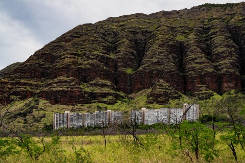 A mountain range with lush greenery towers over a low-rise building in a grassy landscape.