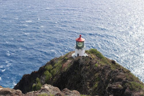 A lighthouse perched on a rocky cliff overlooking the ocean, with waves gently crashing against the shore.