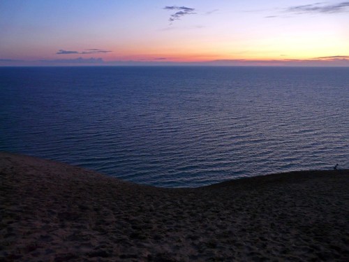A serene sunset over calm waters, with a sandy shoreline in the foreground and a colorful sky above.