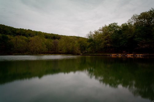 A tranquil lake surrounded by trees, reflecting the cloudy sky and lush greenery on the water's surface.