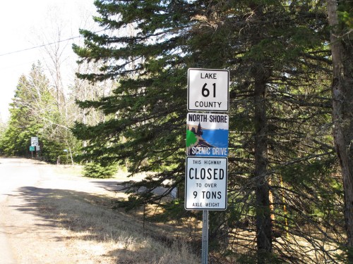 Signpost indicating "North Shore Scenic Drive" and "Closed to over 9 tons axle weight" in a wooded area.