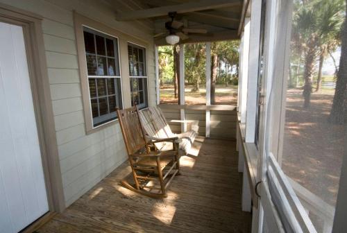 A wooden rocking chair on a porch with a ceiling fan, surrounded by trees and natural light.