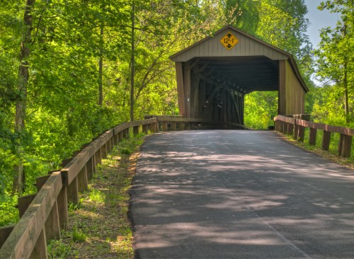 A scenic view of a covered bridge surrounded by lush greenery and a paved road leading to it.