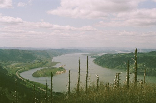 A scenic view of a winding river surrounded by lush green hills and cloudy skies.