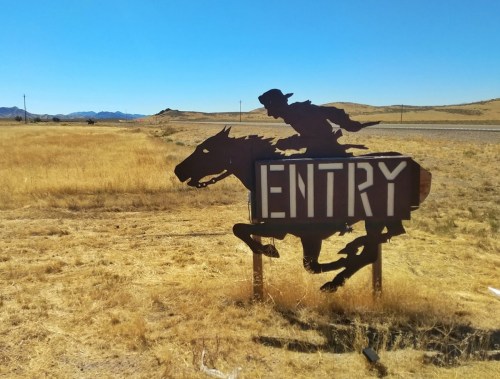 A silhouette of a cowboy riding a horse next to a sign that reads "ENTRY" in a dry, open landscape.