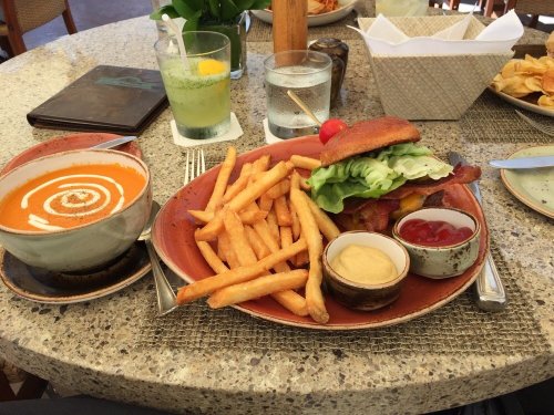 A plate with a burger, fries, and dipping sauces, alongside a bowl of soup and a drink on a table.