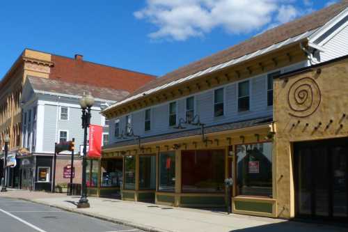 A quiet street scene featuring colorful storefronts and a blue sky with clouds.