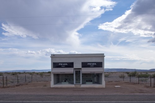 A minimalist Prada storefront in a remote desert landscape under a cloudy sky.