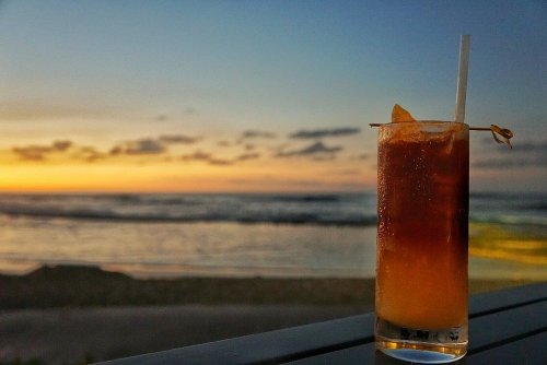 A refreshing drink with ice sits on a table, overlooking a serene beach at sunset.