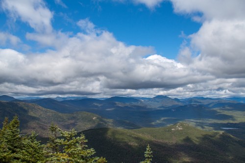 A panoramic view of mountains under a partly cloudy sky, with lush green valleys and distant peaks.