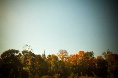 A serene landscape featuring colorful autumn trees under a clear blue sky, with a church steeple in the background.