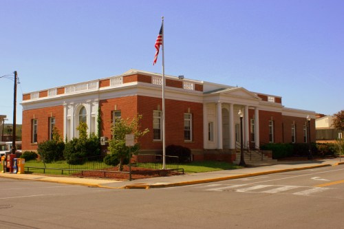 A brick building with white columns, an American flag, and landscaped greenery, set against a clear blue sky.
