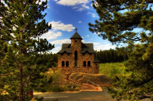 A stone church surrounded by trees, set against a backdrop of blue skies and fluffy clouds.