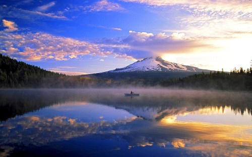 A serene lake at sunrise, with a snow-capped mountain in the background and a lone boat on the calm water.