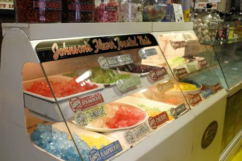 A display of colorful flavored syrups in bowls, labeled with various fruit flavors, at a vintage candy shop.