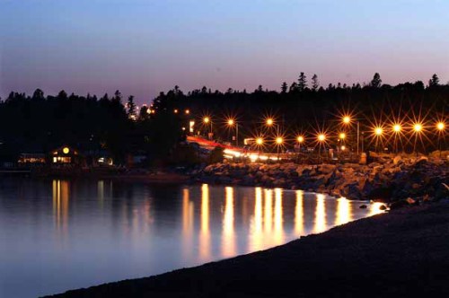 A serene lakeside view at dusk, with shimmering lights reflecting on the water and trees in the background.
