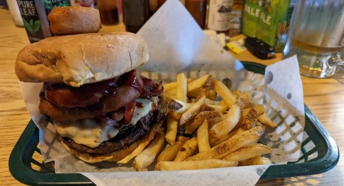 A hearty burger topped with bacon and onion rings, served with a side of golden fries in a basket.