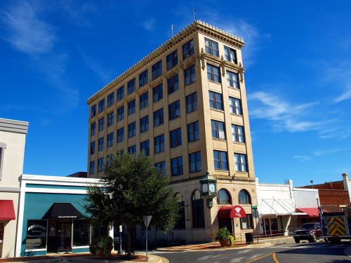 Historic building with a clock tower, surrounded by shops under a clear blue sky.