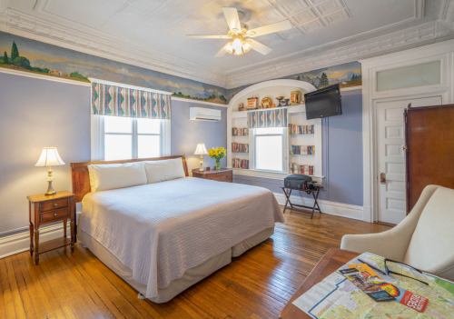 Cozy bedroom with a queen bed, wooden furniture, bookshelves, and a window with colorful curtains.