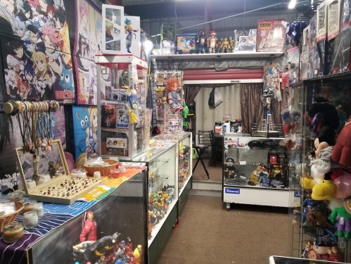 A colorful collectibles shop filled with anime figures, toys, and display cases showcasing various merchandise.