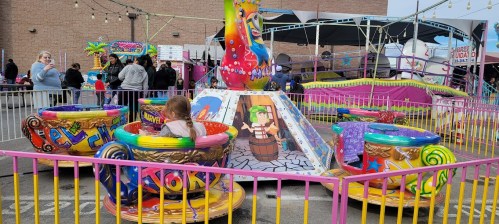 A colorful carnival ride with spinning cups, children enjoying the attraction, and festive decorations in the background.