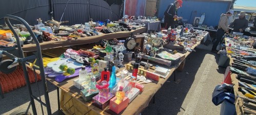A bustling flea market with tables filled with various vintage items, collectibles, and trinkets under a clear blue sky.