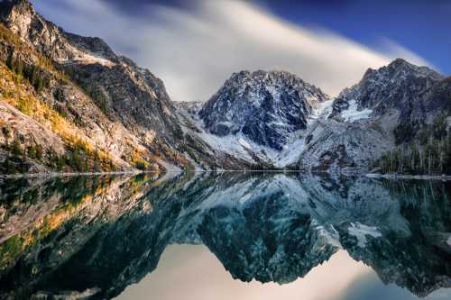 A serene mountain landscape reflecting in calm water, with snow-capped peaks and colorful autumn foliage.