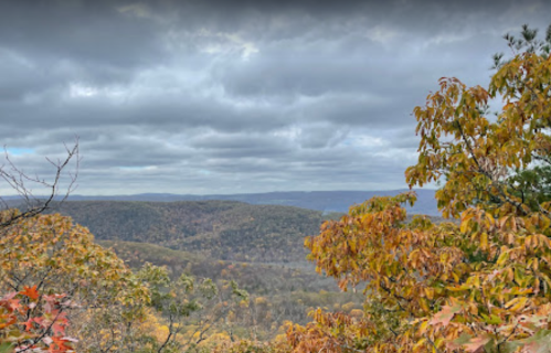 A scenic view of rolling hills covered in autumn foliage under a cloudy sky.