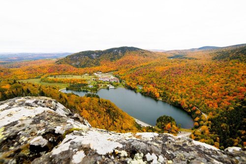 Aerial view of a vibrant autumn landscape with colorful trees surrounding a serene lake and rolling hills.
