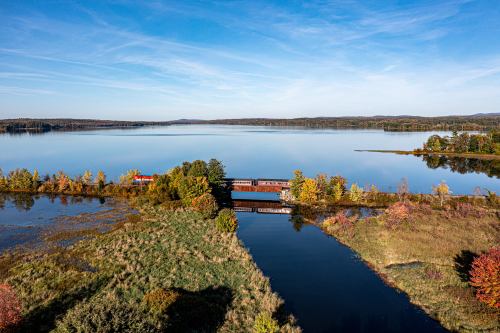 A serene landscape featuring a calm lake, a train bridge, and colorful autumn foliage under a clear blue sky.