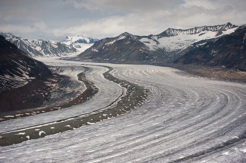 A sweeping view of a glacier winding through rugged mountains under a cloudy sky.