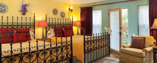 Cozy bedroom with two iron beds, colorful walls, decorative pillows, and a seating area by a door leading outside.